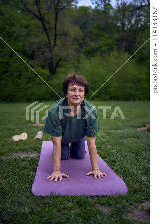 old woman practices yoga in the morning on the river bank, came from home by bicycle 114133167