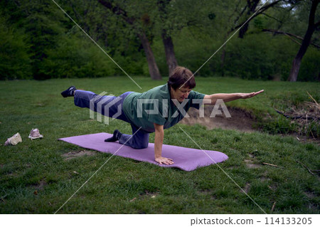 old woman practices yoga in the morning on the river bank, came from home by bicycle 114133205