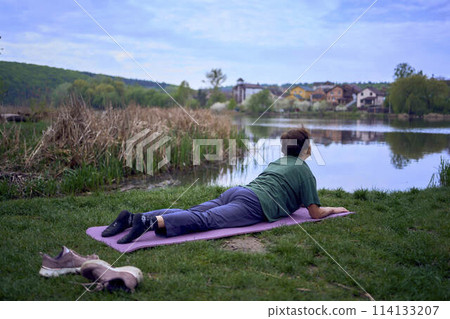 old woman practices yoga in the morning on the river bank, came from home by bicycle 114133207