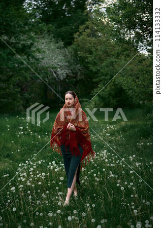 Slavic girl in a scarf on the grass with dandelions 114133332