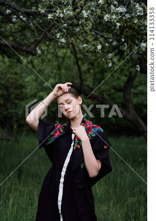Slavic girl in a scarf near blooming apple trees 114133358