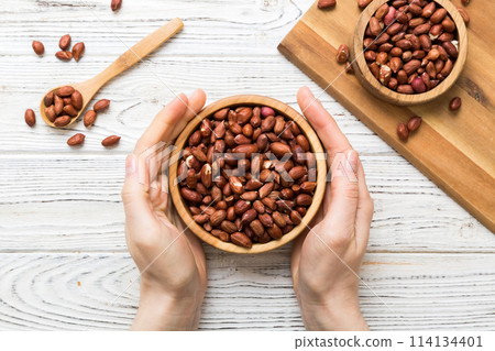 Woman hands holding a wooden bowl with peanuts. Healthy food and snack. Vegetarian snacks of different nuts Woman hands holding a wooden bowl with peanuts. Healthy food and snack. Vegetarian snacks of different nuts 114134401