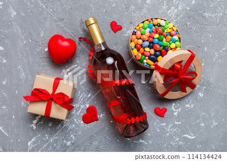 Bottle of red wine on colored background for Valentine Day with gift and chocolate. Heart shaped with gift box of chocolates top view with copy space 114134424
