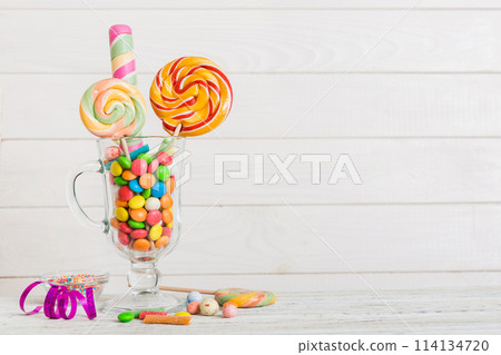 Colorful candies in cup on table on light background background. Large swirled lollipops. Creative concept of a jar full of delicious sweets from the candy store Colorful candies in cup on table on light background background. Large swirled lollipops. Creative concept of a jar full of delicious sweets from the candy store 114134720