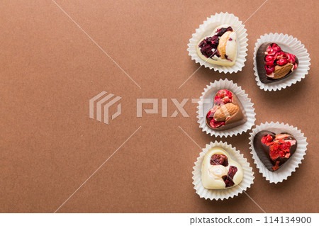 chocolate sweets in the form of a heart with fruits and nuts on a colored background. top view with space for text, holiday concept chocolate sweets in the form of a heart with fruits and nuts on a colored background. top view with space for text, holiday concept 114134900