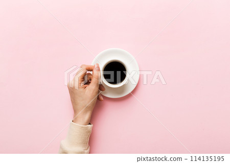 Minimalistic style woman hand holding a cup of coffee on Colored background. Flat lay, top view cappuccino cup. Empty place for text, copy space. Coffee addiction. Top view, flat lay 114135195