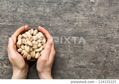 Woman hands holding a wooden bowl with pistachios nuts. Healthy food and snack. Vegetarian snacks of different nuts 114135225