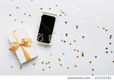 Opened gift box with gold ribbon and smartphone on color background, top view. Blank open box packaging mockup , Template for your design - branding mockup 114135382