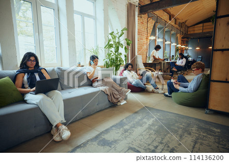 Dynamic workday. Young multiethnic people meeting in co-working environment, showing bustling activity that characterizes modern workspaces. 114136200
