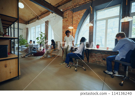 Interactive co-working space. Bustling co-working environment with young multiethnic people working and studying Interactive co-working space. Bustling co-working environment with young multiethnic people working and studying 114136240