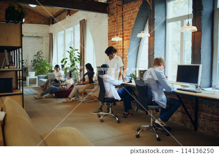 Productive coworking. Young people in modern office, maintaining productivity, working on gadgets. Positive ad comfortable atmosphere 114136250