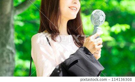 Woman cooling off with a handheld fan - summer heatstroke prevention Woman cooling off with a handheld fan - summer heatstroke prevention 114136308