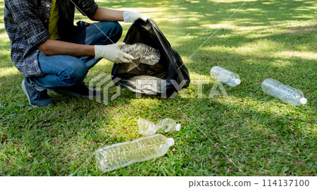 Hand holding plastic bottle waste, picking up trash and putting it in the black garbage bag at the Park on Environmental Earth day 114137100