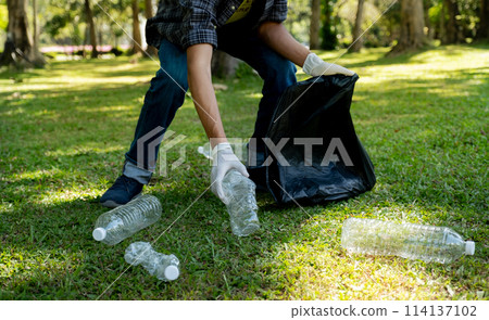 Hand holding plastic bottle waste, picking up trash and putting it in the black garbage bag at the Park on Environmental Earth day 114137102