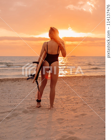 Surfgirl with blonde long hair go to surfing. Woman holding surfboard on a beach at sunset or sunrise. Surfer and ocean 114137476