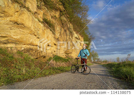 senior male cyclist riding a folding bike on Steamboat Trace, bike trail converted from an abandoned railroad, near Peru, Nebraska, springtime morning scenery 114138075