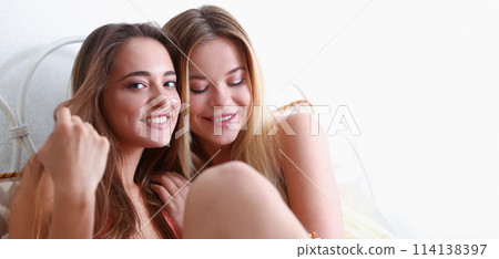 Two happy smiling girlfriends eat popcorn in bed Two happy smiling girlfriends eat popcorn in bed 114138397
