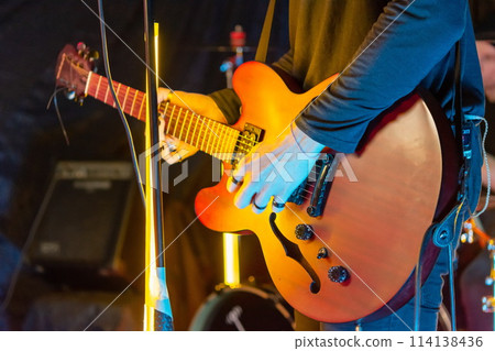 Musician playing orange semi-hollow body electric guitar on stage with yellow lights in background 114138436