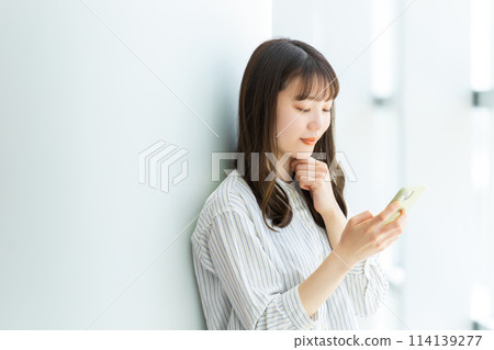 Smiling young woman using a smartphone 114139277