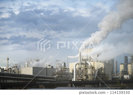 Industrial Factory Emits Smoke Against Cloudy Sky Industrial Factory Emits Smoke Against Cloudy Sky 114139330
