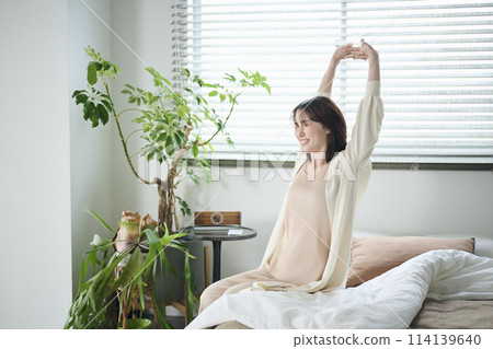 A woman in her twenties wakes up and stretches in bed 114139640