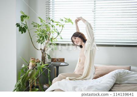 A woman in her twenties wakes up and stretches in bed 114139641