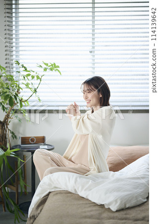A woman in her twenties wakes up and stretches in bed 114139642