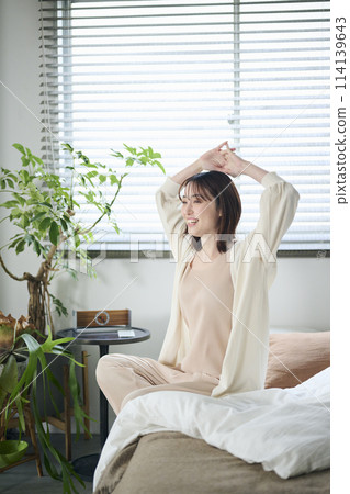A woman in her twenties wakes up and stretches in bed 114139643