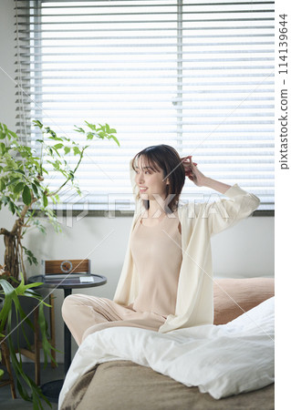 A woman in her twenties wakes up and stretches in bed 114139644