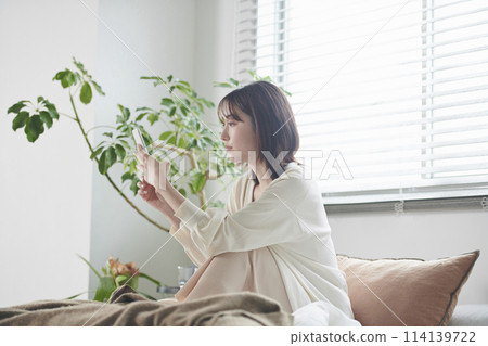 A woman in her twenties looking at her smartphone in bed 114139722