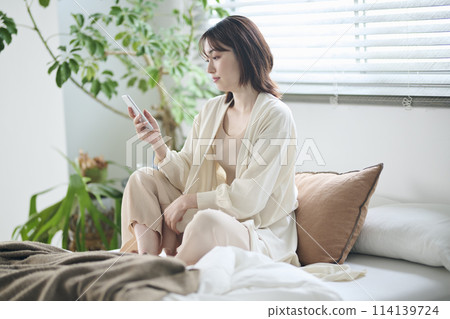 A woman in her twenties looking at her smartphone in bed 114139724