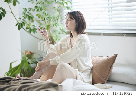 A woman in her twenties looking at her smartphone in bed A woman in her twenties looking at her smartphone in bed 114139725