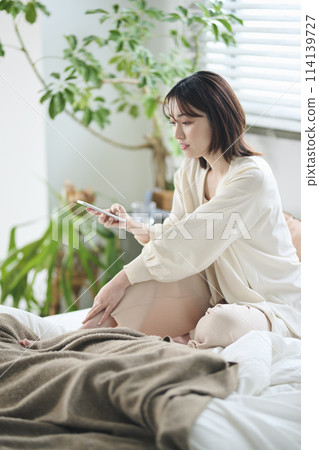 A woman in her twenties looking at her smartphone in bed A woman in her twenties looking at her smartphone in bed 114139727