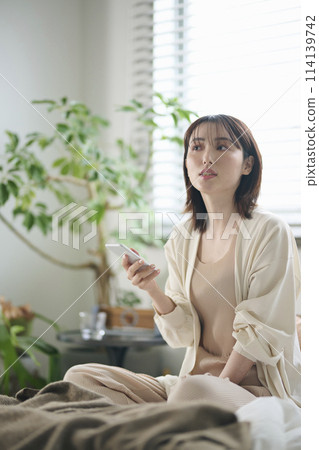 A woman in her twenties looking at her smartphone in bed 114139742