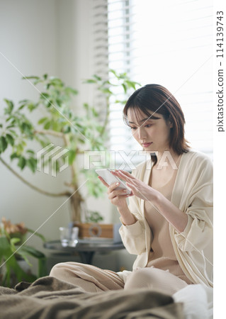 一名 20 多歲的女性躺在床上看智慧型手機 114139743