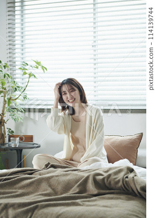 A woman in her 20s sitting on a bed A woman in her 20s sitting on a bed 114139744