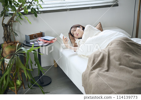 A woman in her twenties lying in bed and looking at her smartphone 114139773