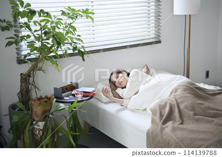 A woman in her twenties lying in bed and looking at her smartphone 114139788