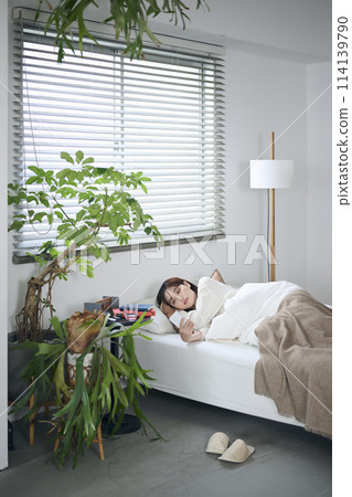 一名 20 多歲的女性躺在蒲團上,看著她的智慧型手機 一名 20 多歲的女性躺在蒲團上,看著她的智慧型手機 114139790