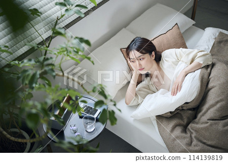 A woman in her twenties wakes up and looks at the clock 114139819