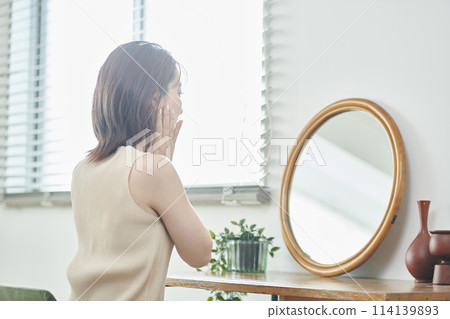 A woman in her twenties doing skin care in front of a mirror 114139893