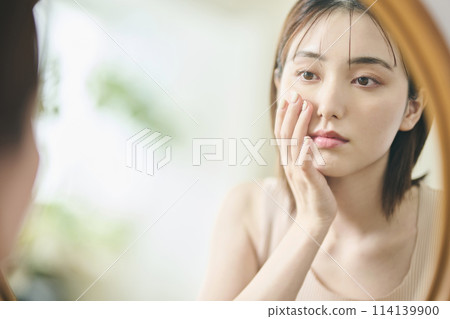 一名20多歲的女性對著鏡子做護膚 114139900