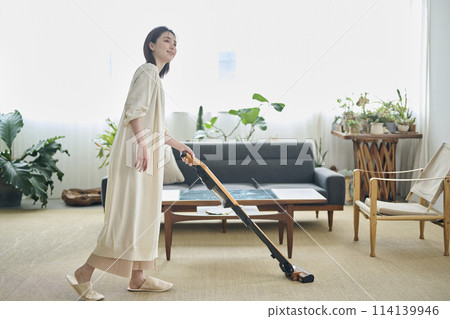 A woman in her twenties vacuuming in the living room 114139946