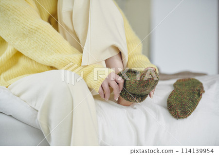 The hands of a woman in her twenties trying to put on socks on the bed 114139954