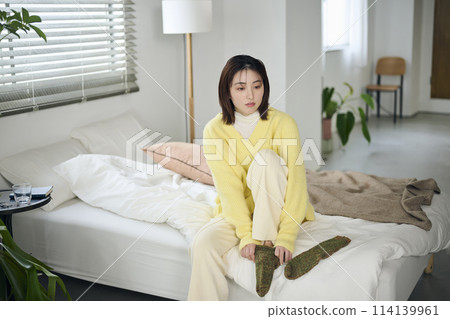A woman in her twenties trying to put on socks on her bed 114139961