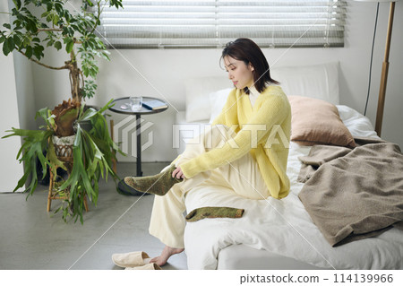 一名20多歲的女性試圖在床上穿上襪子 一名20多歲的女性試圖在床上穿上襪子 114139966