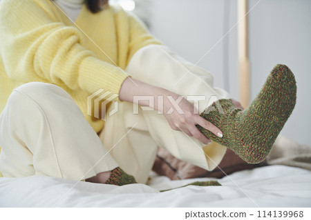 一名 20 多歲的女性試圖在床上穿襪子的手 一名 20 多歲的女性試圖在床上穿襪子的手 114139968