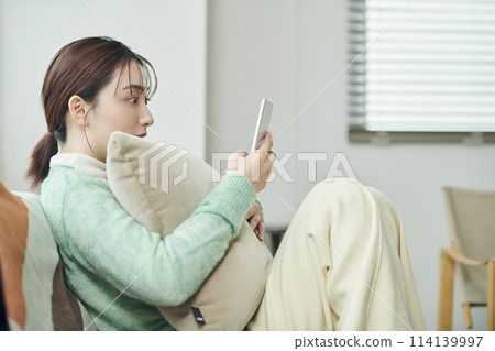 一位女士在沙發上放鬆時看著平板電腦 114139997