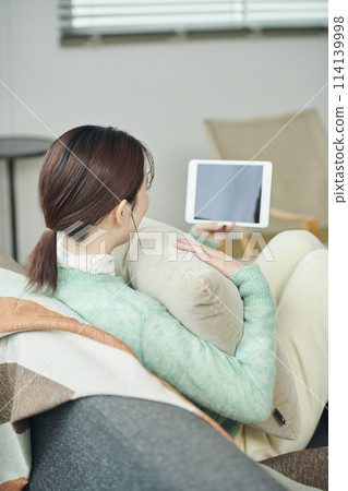 一位女士在沙發上放鬆時看著平板電腦 114139998