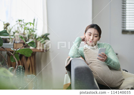 Woman relaxing on sofa and looking at smartphone 114140035